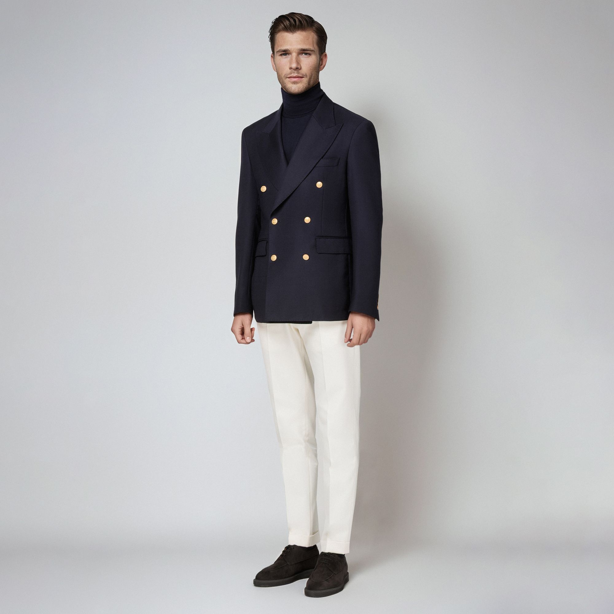 Άνδρας με total look Elio Evan: navy σταυρωτό blazer με χρυσά κουμπιά, μπλε ζιβάγκο και λευκό παντελόνι.