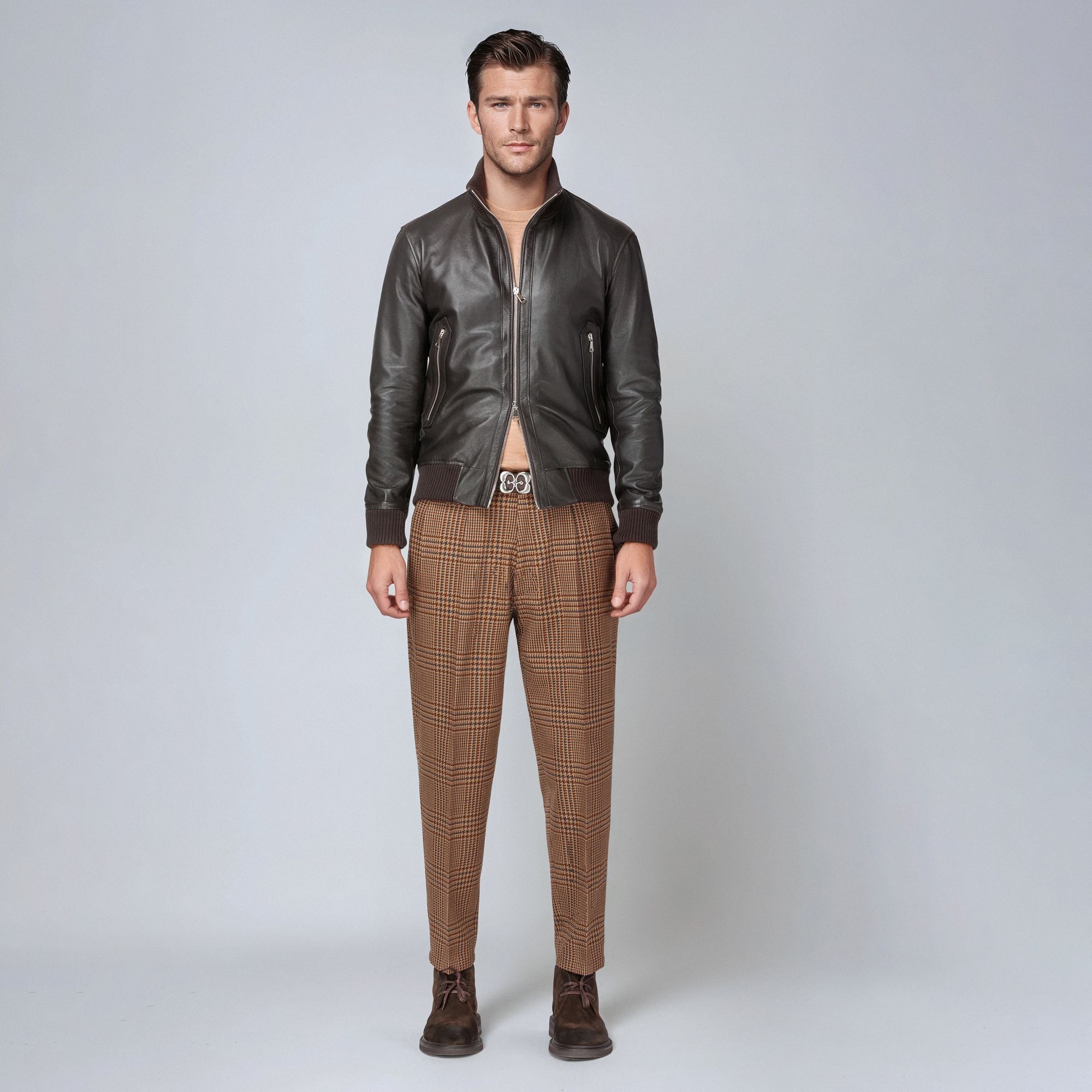 Άνδρας με total look Elio Evan: καφέ δερμάτινο bomber, καφέ καμηλό πλεκτό πουλόβερ από μαλλί merinos, καρό μάλλινο παντελόνι wide fit cropped και καφέ σουέντ μποτάκια.